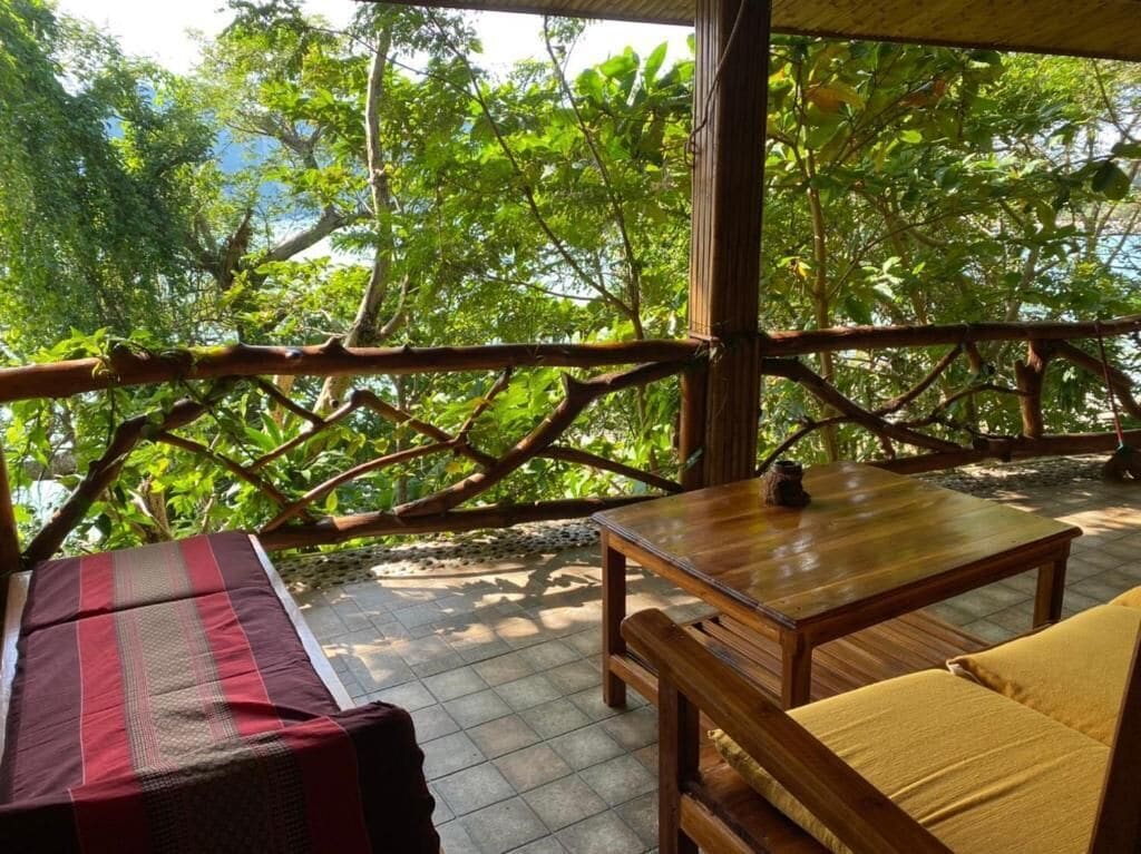 A wooden deck with a sofa and table, surrounded by lush greenery.