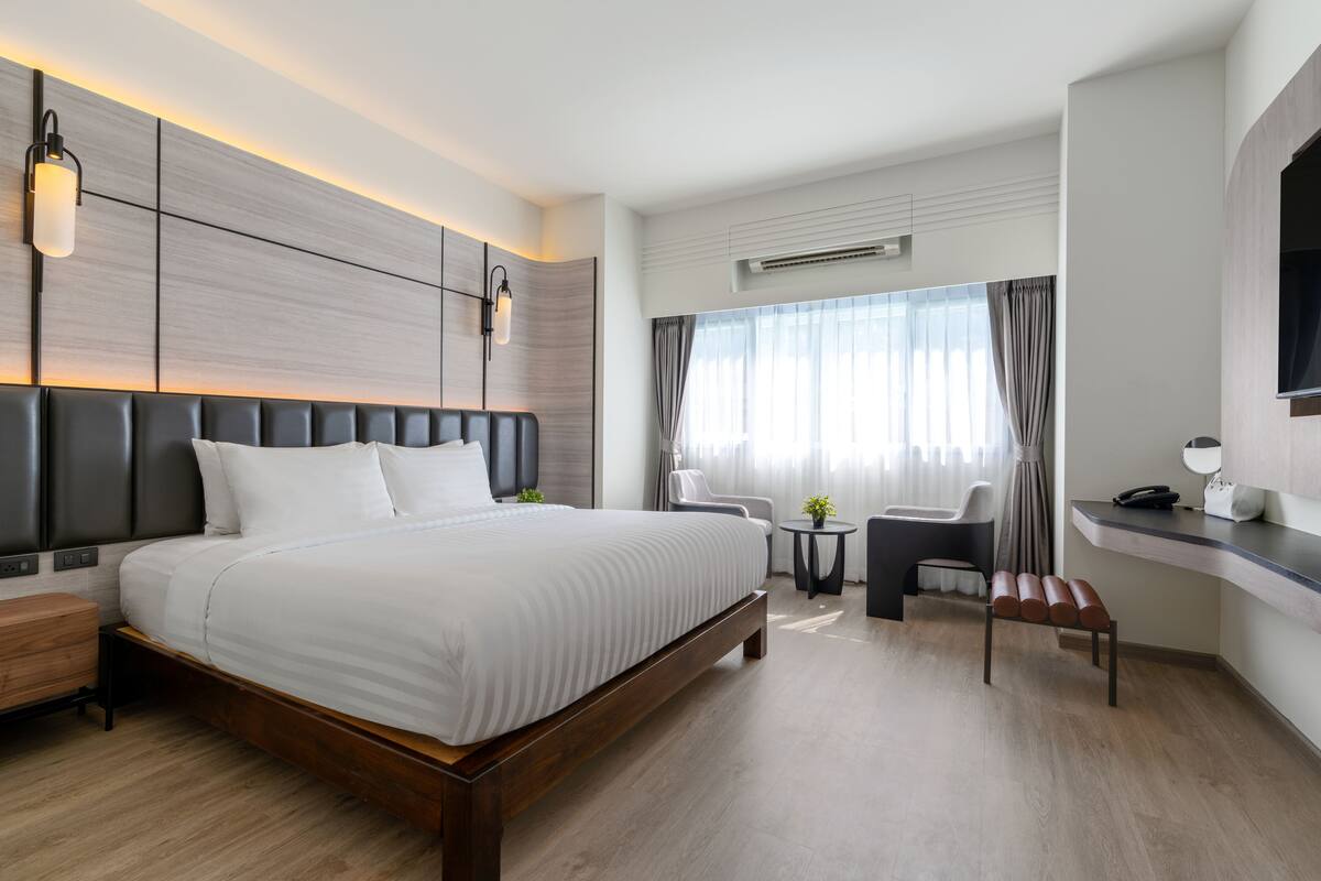 A modern hotel room with a large bed, a desk, a chair, and a small table with a plant.