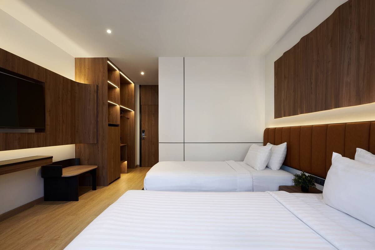A modern hotel room with two beds, a TV, wooden paneling, and built-in closets.
