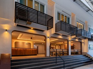 A hotel lobby with a reception desk, a staircase leading to a balcony, and a second-floor balcony with a railing. - Panmanee Hotel (Ko Phi Phi)