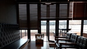 Un restaurante con mesa de madera, asientos tipo banca de cuero negro y ventanas amplias con persianas.