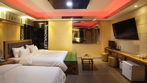 Habitación de hotel con dos camas, un banco verde, una mesita pequeña, un televisor y un minibar.