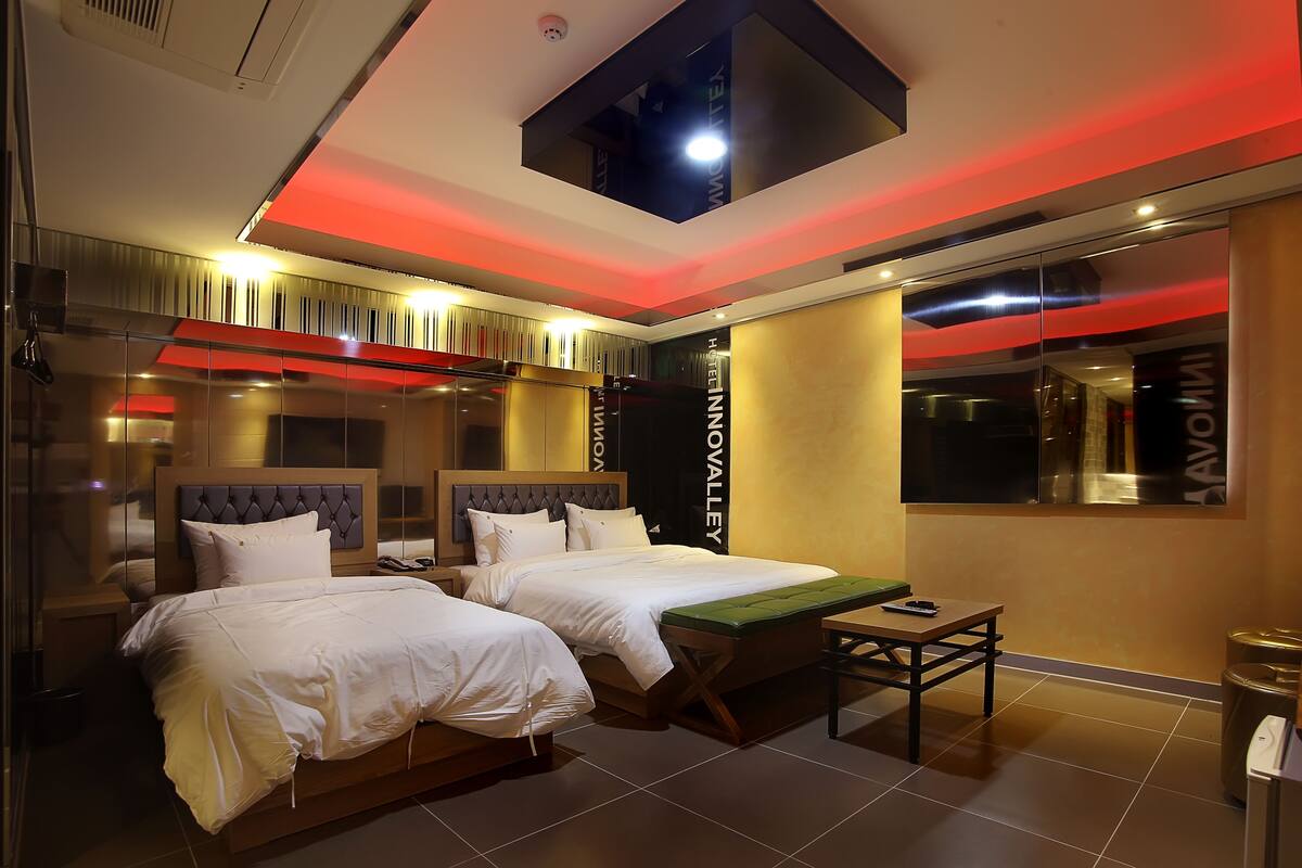 A hotel room with two beds, a small table, and a view of the city.