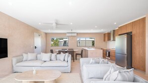 A modern living room with a sofa, a coffee table, and a dining area with a table and chairs. - Hastings House (Noosa Heads)