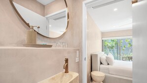 A modern bathroom with a large oval sink, a round mirror, and a bedside table with a mattress. - Hastings House (Noosa Heads)