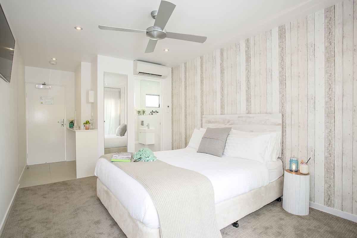 Ein Schlafzimmer mit Bett, Deckenventilator, Nachttisch, Spiegel und Kleiderschrank.