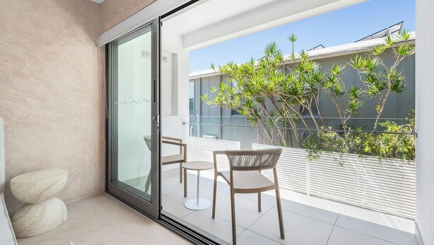 A modern balcony with a glass door, a small table, two chairs, and a potted plant. - Hastings House (Noosa Heads)