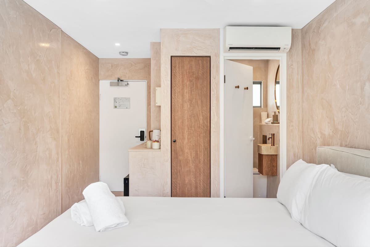 Ein Hotelzimmer mit einem Bett, einer Holztür, einem Badezimmer mit Waschbecken und einer Klimaanlage.