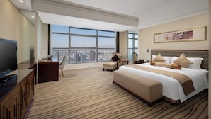 Quarto de hotel com uma cama grande, uma televisão, uma escrivaninha e uma cadeira.