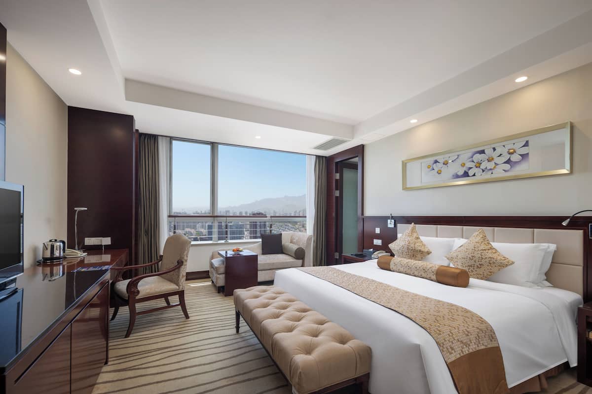Habitación de hotel con una cama grande, un escritorio, una silla, un banco y un televisor.