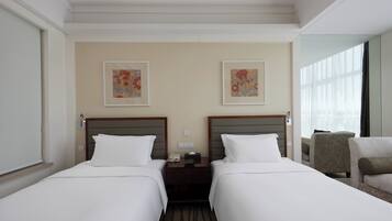 Habitación de hotel con dos camas, una mesita de noche, una silla y dos cuadros con motivos florales en la pared.