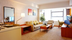Habitación de hotel con sofá, mesa de centro, sillón, escritorio y un ventanal grande.