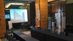 Una sala de conferencias con una larga mesa, sillas, una pantalla de proyector y una presentación.