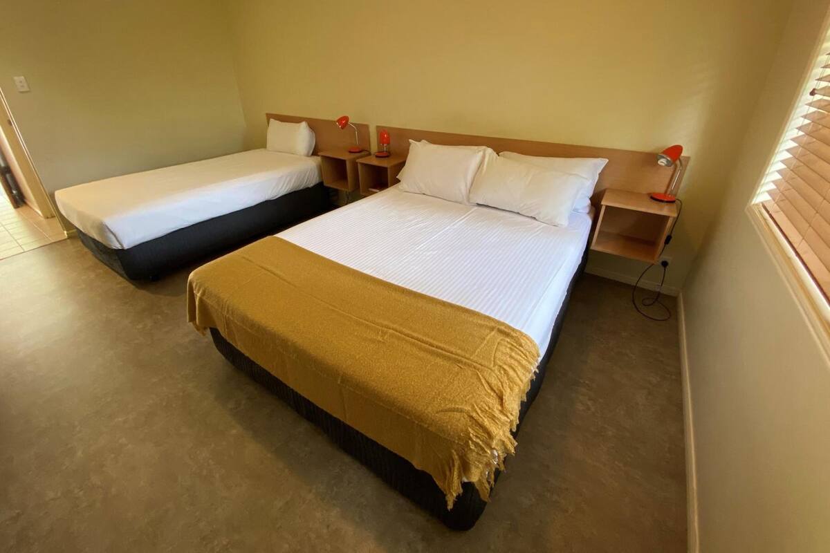 A hotel room with two single beds, a large bed, and a wooden headboard.
