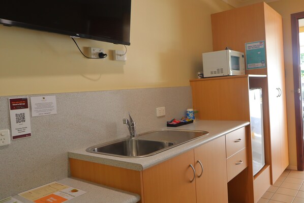A kitchen with a stainless steel sink, wooden cabinets, a microwave, and a refrigerator.