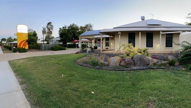A building with a covered outdoor area, a sign with a logo, and a landscaped garden with rocks and shrubs. - Country Roads Motor Inn Gayndah Qld (Gayndah)