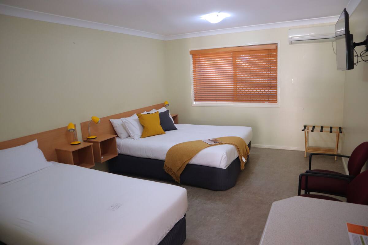 A hotel room with two single beds, a desk, a chair, and a window with blinds.