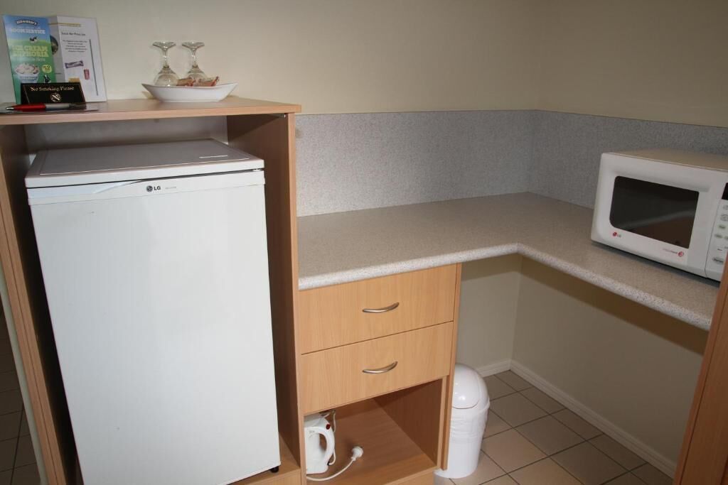 A compact kitchenette with a white refrigerator, microwave, and a small cabinet with drawers.