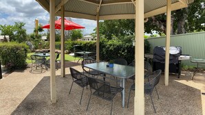 An outdoor patio with tables and chairs, a barbecue grill, and a red umbrella. - Country Roads Motor Inn Gayndah Qld (Gayndah)