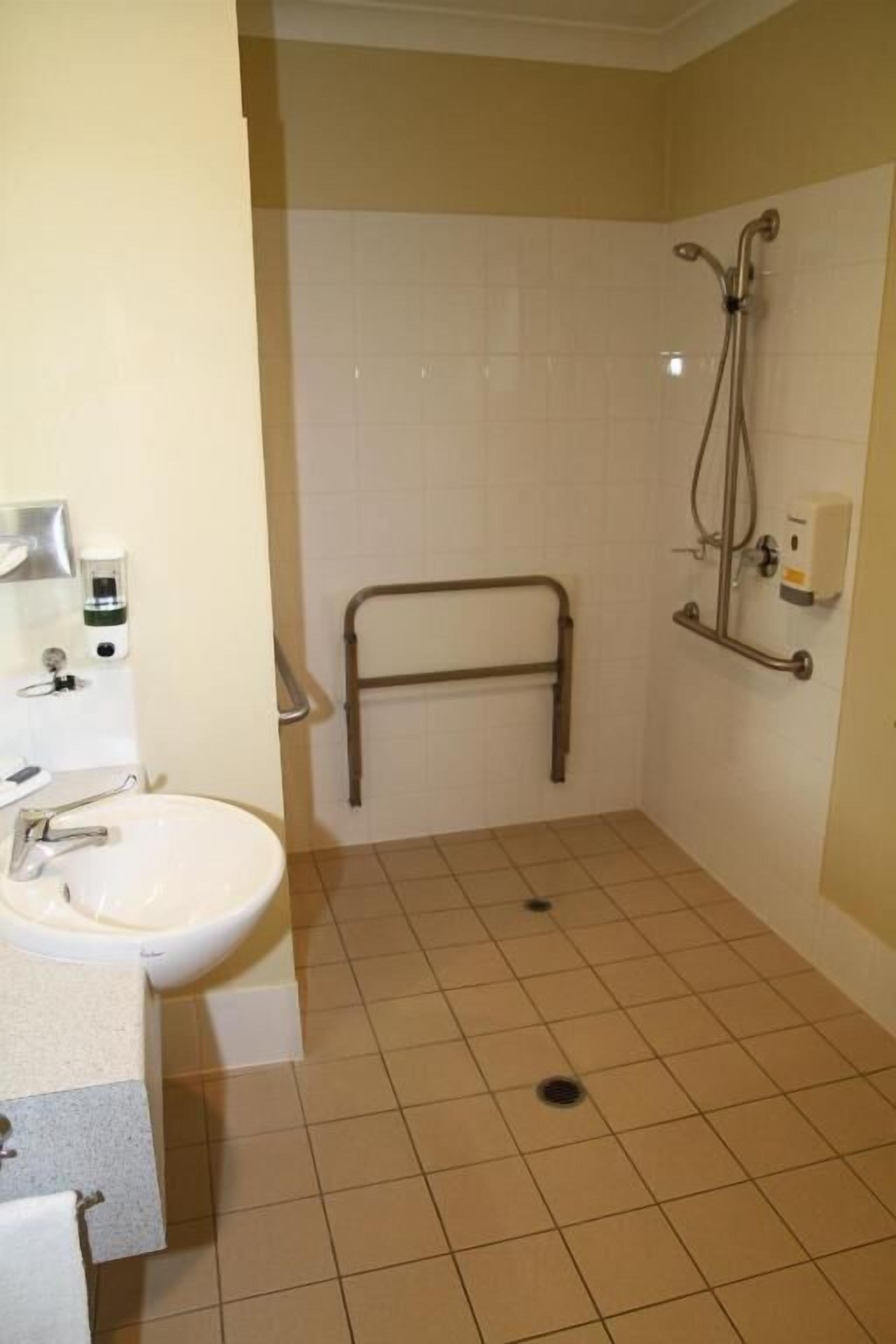 Un bagno con lavandino, erogatore di sapone per le mani e doccia dotata di maniglione.