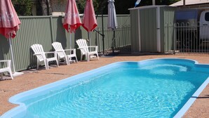 A rectangular swimming pool with a light blue interior, surrounded by white chairs and pink umbrellas. - Country Roads Motor Inn Gayndah Qld (Gayndah)
