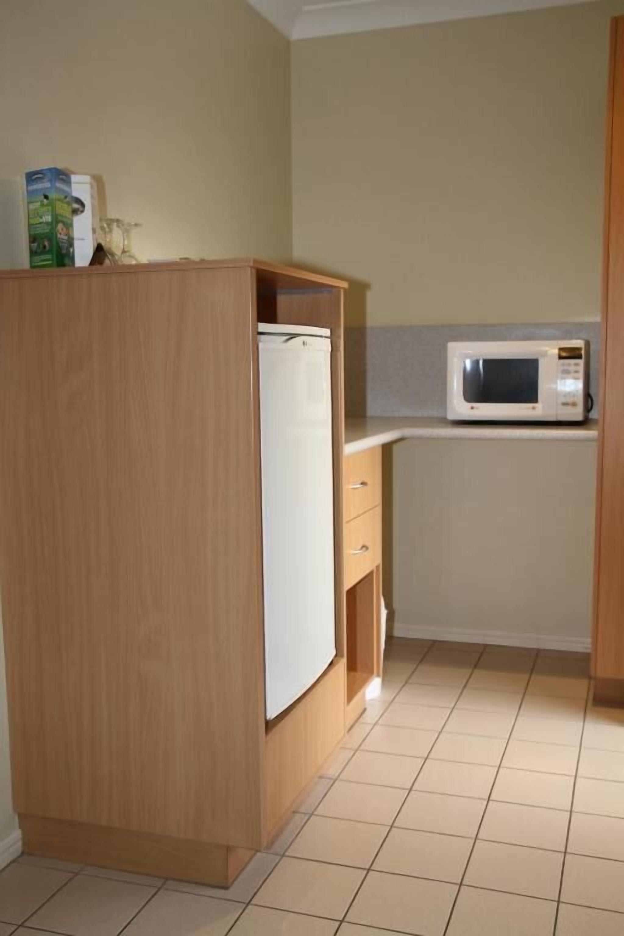 A compact kitchen with a microwave, a small refrigerator, and wooden cabinets.