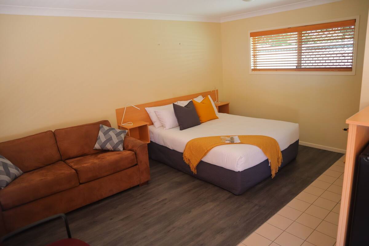 A bedroom with a bed, a sofa, and a window with blinds.