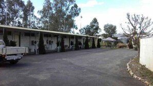 A single-story building with a covered outdoor area, likely a motel or small hotel, with a paved driveway and parked vehicles.