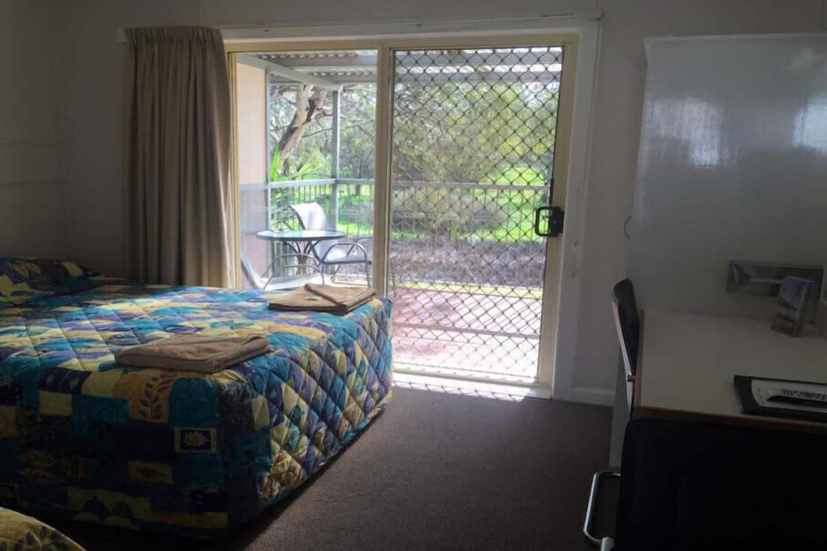 A bedroom with a bed, a desk, and a view of a patio with a table and chairs.