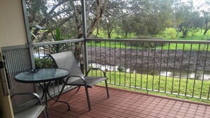 A balcony with a table and chairs, overlooking a grassy area and a body of water.