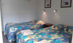 A small, simple room with two beds, each covered with a colorful quilt. There are two wall-mounted lights above the beds.