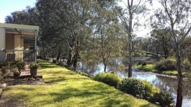 A riverside property with a grassy lawn, trees, and a building with a balcony.