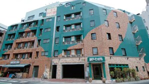 A multi-story building with a mix of brick and teal facades, featuring a ground-level entrance with a sign. - Urban Hotel Tokyo Fuchu-Higashiguchi (Fuchu)