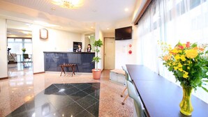 A hotel lobby with a reception desk, a large window with flowers, and a tiled floor. - Urban Hotel Tokyo Fuchu-Higashiguchi (Fuchu)