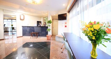 Un vestíbulo de hotel con una recepción, un amplio ventanal con flores y un suelo de baldosas.