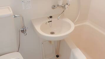 A bathroom with a toilet, sink, and bathtub. There are toiletries on a shelf above the sink.
