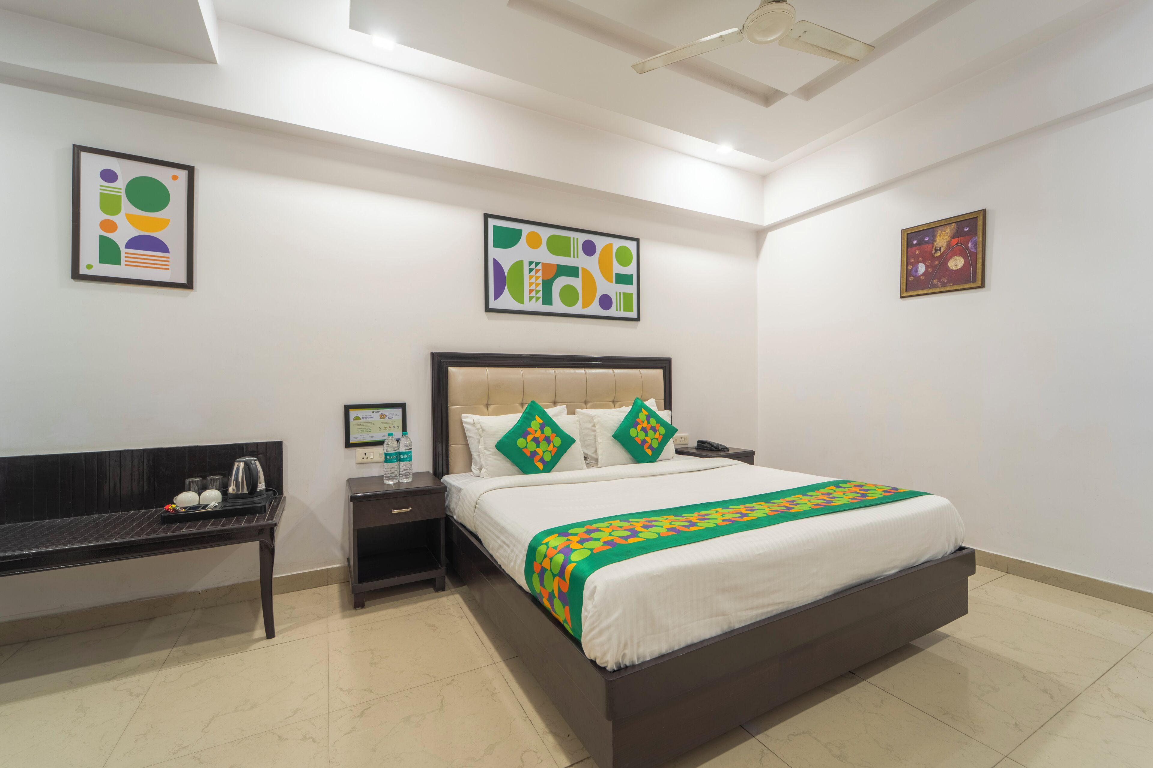 A hotel room with a bed, bedside tables, a bench, and artwork on the walls.