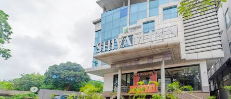 A modern hotel with a prominent sign reading "SHIVAI HOTEL" and "treebo Shyamini Inn" on the facade. There are potted plants and a staircase leading to the entrance.