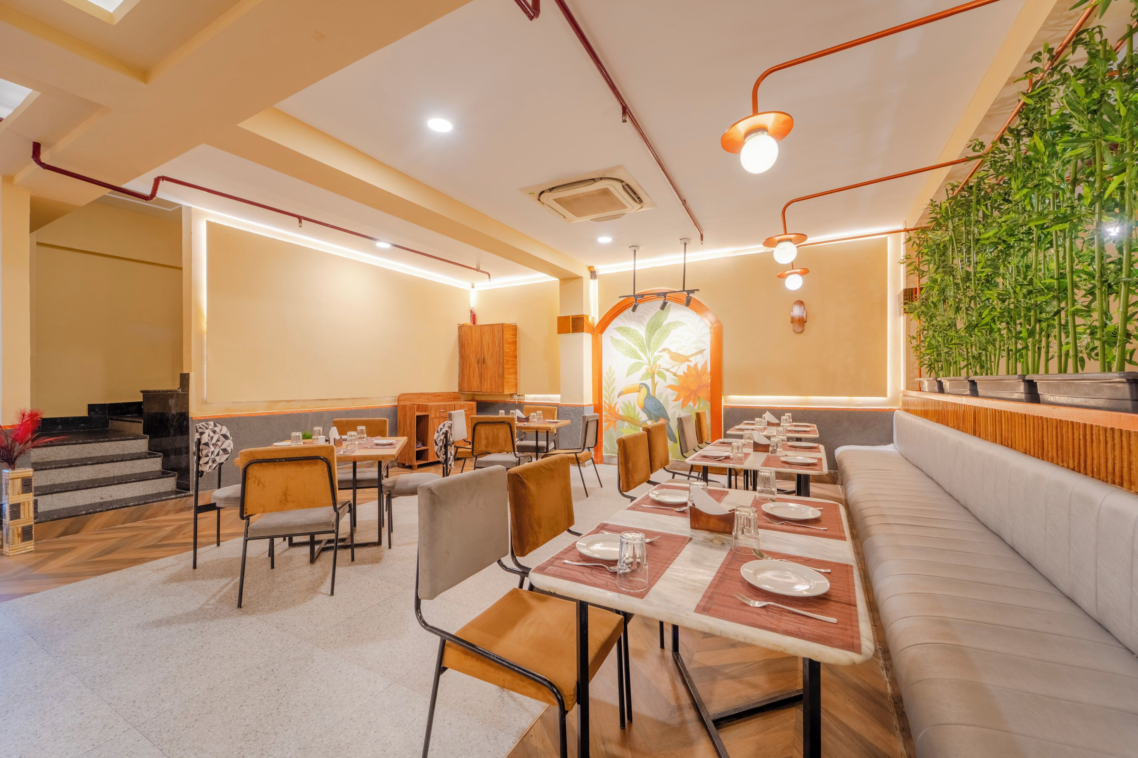 A restaurant with multiple tables and chairs, a staircase, and a wall with a bamboo plant.