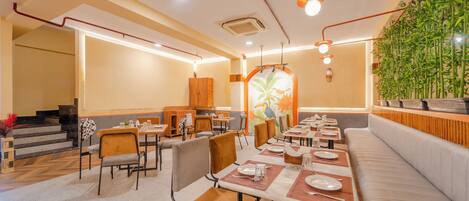 A restaurant with multiple tables and chairs, a staircase, and a wall with a bamboo plant.