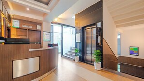 A reception area with a wooden desk, a reception counter, a staircase, and potted plants. - Treebo Shivam Inn Near Singapore Mall (Lucknow)