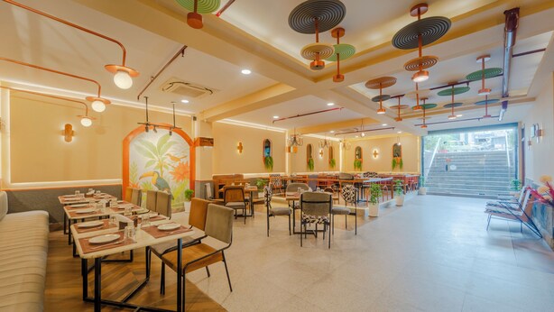 A spacious restaurant with multiple dining areas, a staircase leading to an outdoor area, and a variety of seating options including tables and chairs. - Treebo Shivam Inn Near Singapore Mall (Lucknow)