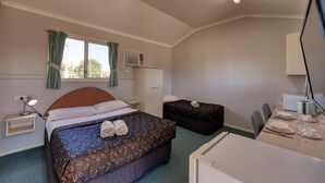 A hotel room with a single bed, a desk with a chair, a window with curtains, and a small kitchenette. - Matilda Motel (Winton)