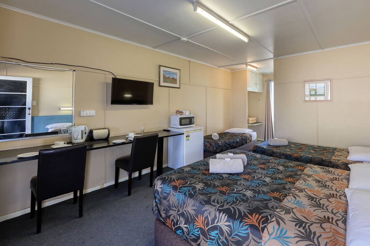 A hotel room with a desk, two beds, a TV, a microwave, and a small window.
