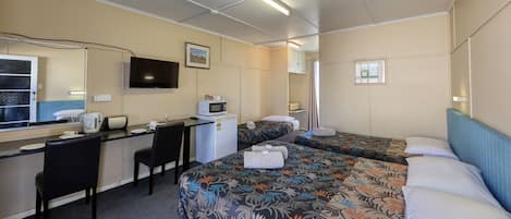 A hotel room with a desk, two beds, a TV, a microwave, and a small window.