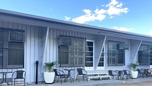A building with a row of outdoor tables and chairs, large potted plants, and a covered walkway. - Matilda Motel (Winton)