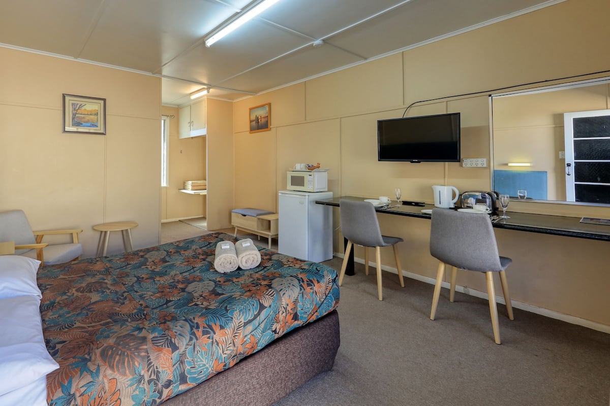 A hotel room with a bed, a desk, a chair, a TV, and a microwave.