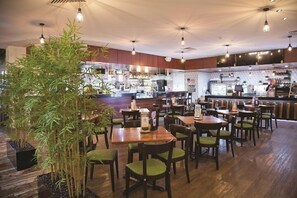 Un restaurante con mesas y sillas de madera, una zona de bar y plantas de bambú.