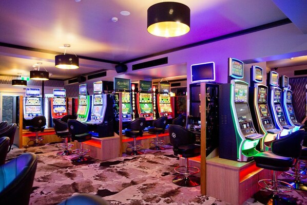 Zona de juegos con varias máquinas recreativas y sillones.