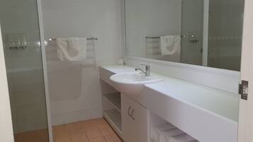 Un baño con lavamanos blanco, un espejo y una zona de ducha.